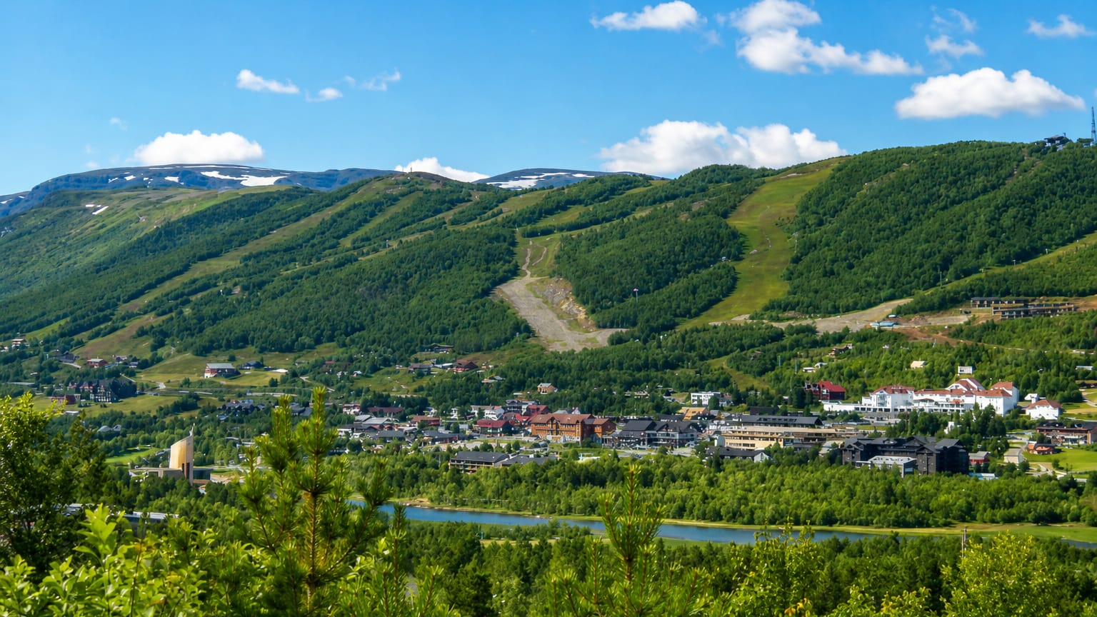 Geilo town centre in a green summer valley below forested mountains with ski slopes and a river, Norway.