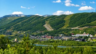 Geilo town centre in a green summer valley below forested mountains with ski slopes and a river, Norway.