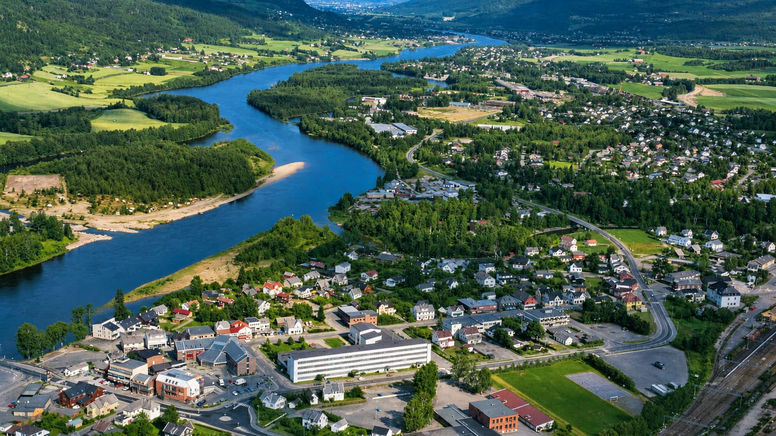 Aerial view of Hokksund, Norway, a riverside town along the Drammenselva winding through a green valley framed by forested hills.