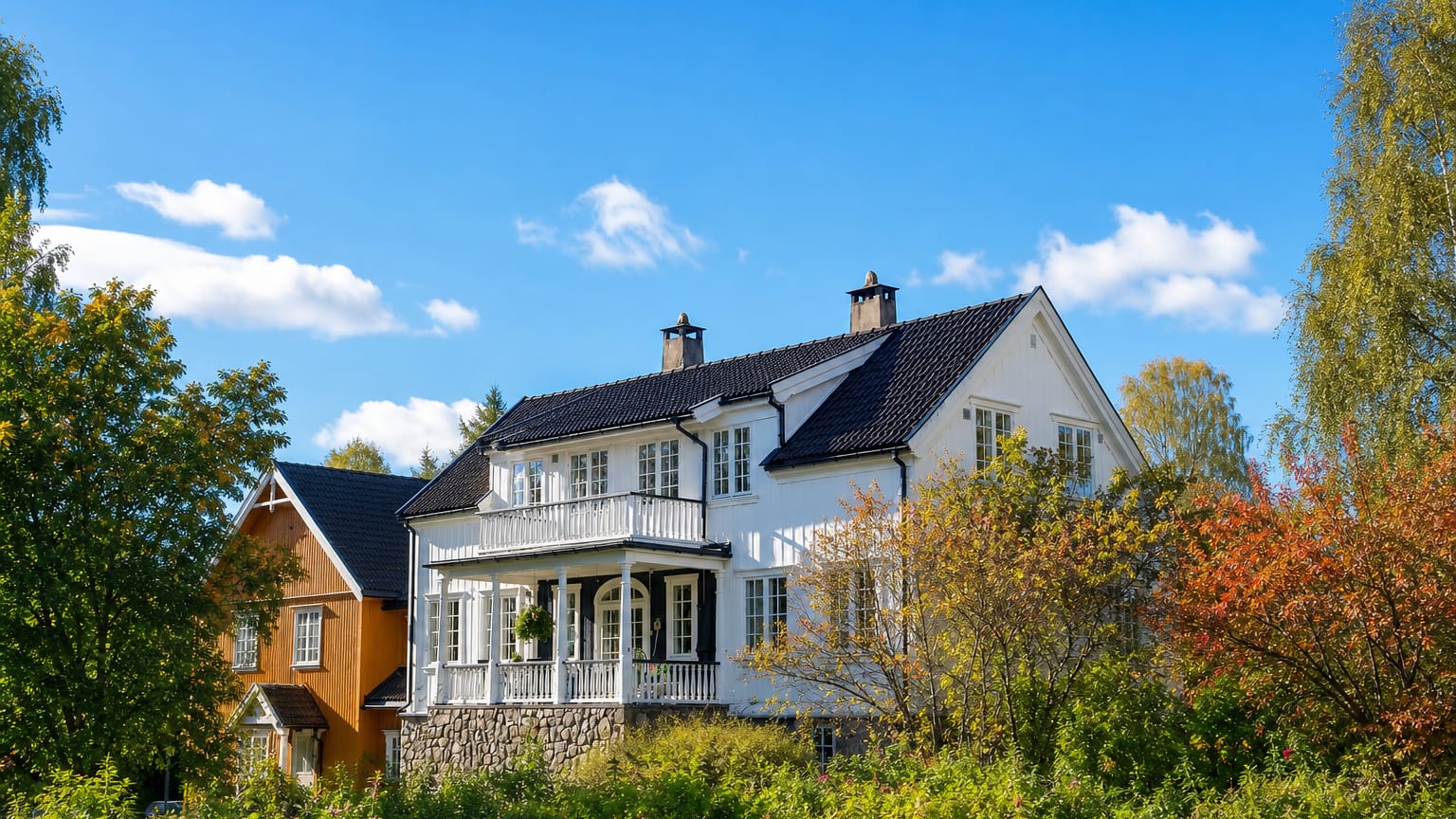 A white wooden villa with a balcony stands among autumn-tinged trees in Lampeland, Norway.