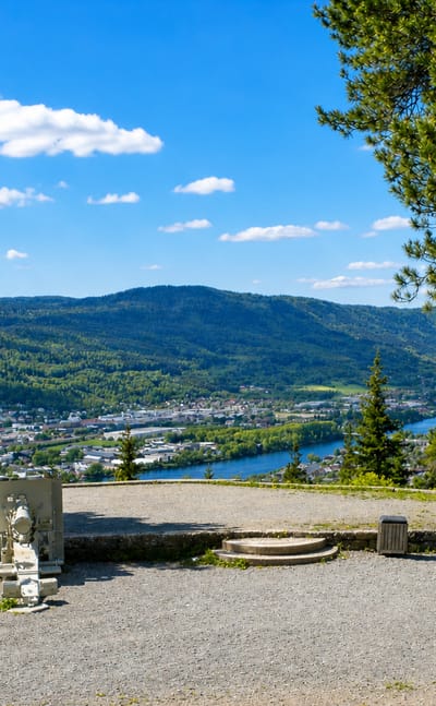 Hillside viewpoint over the Lier valley with a river and Lierbyen spread below forested ridges, Buskerud, Norway.