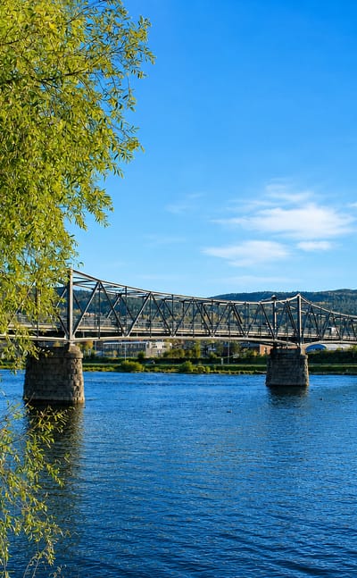 Truss footbridge crossing the river with the town of Mjondalen, Norway, on the far bank.