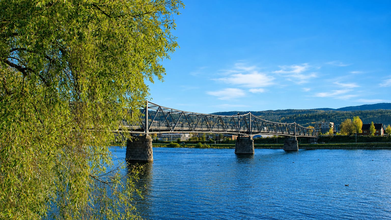 Truss footbridge crossing the river with the town of Mjondalen, Norway, on the far bank.