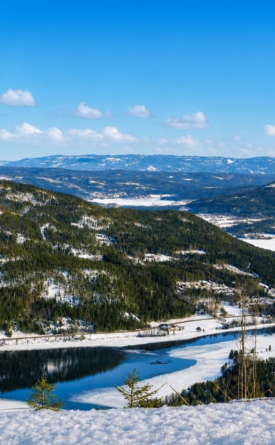 Snowy forested valley above a partly frozen lake under a blue sky near Noresund, Buskerud, Norway