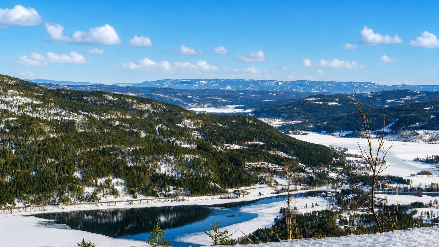 Snowy forested valley above a partly frozen lake under a blue sky near Noresund, Buskerud, Norway