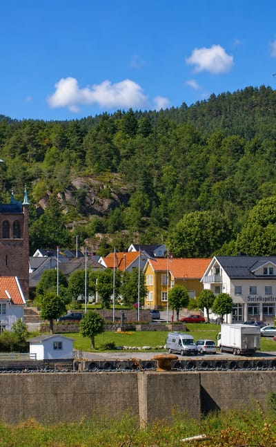 Brick church with a green spire above the town and forested hills at Svelvik, Norway