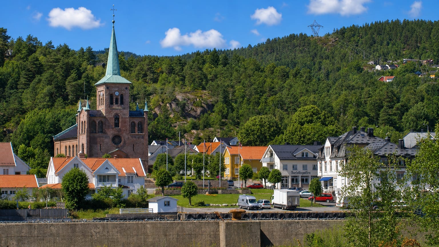 Brick church with a green spire above the town and forested hills at Svelvik, Norway