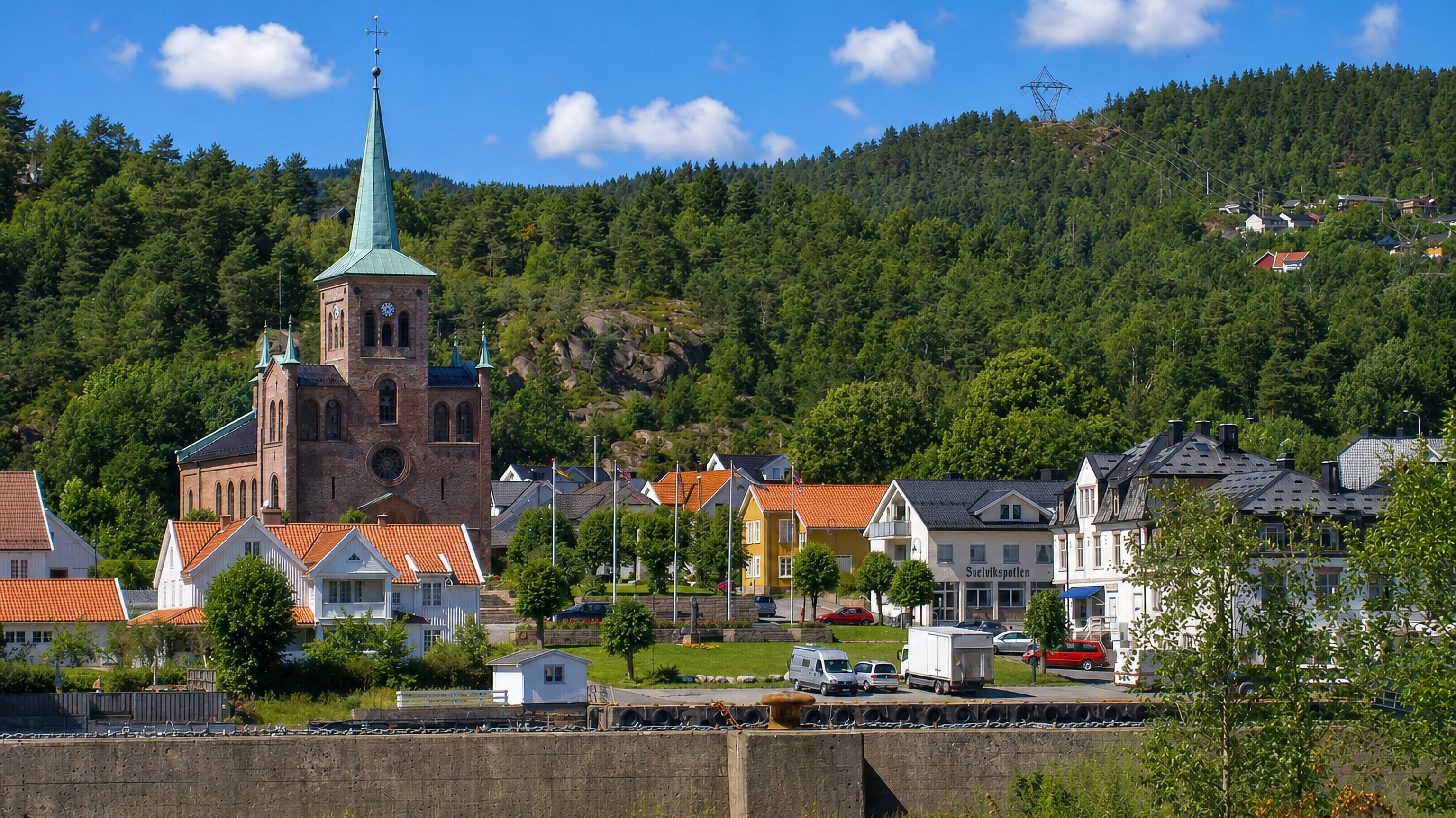 Brick church with a green spire above the town and forested hills at Svelvik, Norway