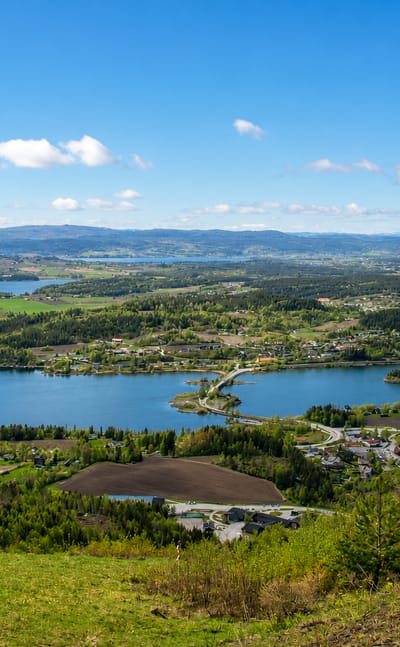 Elevated daytime panorama over Vik, Norway, overlooking Tyrifjorden's wooded islands, farmland and distant blue hills.