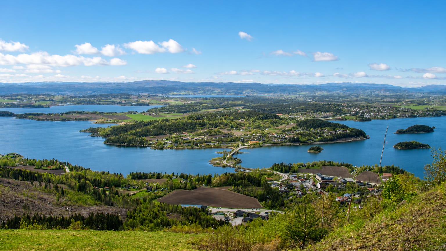 Elevated daytime panorama over Vik, Norway, overlooking Tyrifjorden's wooded islands, farmland and distant blue hills.