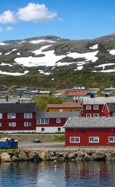 Colourful fishing-village houses on the waterfront below a snow-patched fell in Båtsfjord, Norway