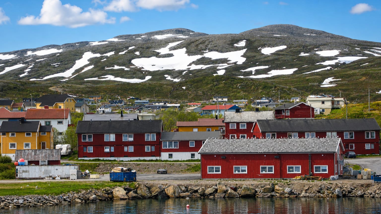 Colourful fishing-village houses on the waterfront below a snow-patched fell in Båtsfjord, Norway