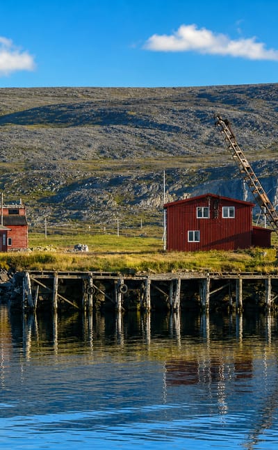 Berlevåg, Norway, red waterfront buildings and an old wharf crane below barren tundra hills in Finnmark.