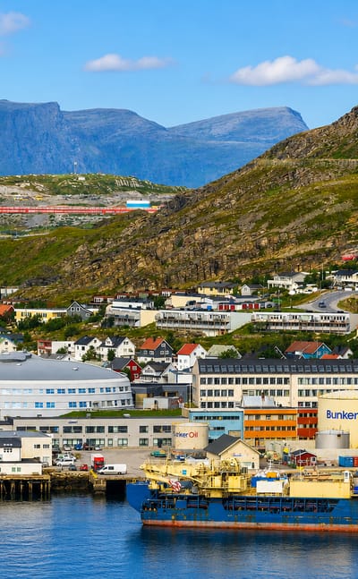 Waterfront town of Hammerfest, Norway, below barren mountains with harbour vessels and a radio mast