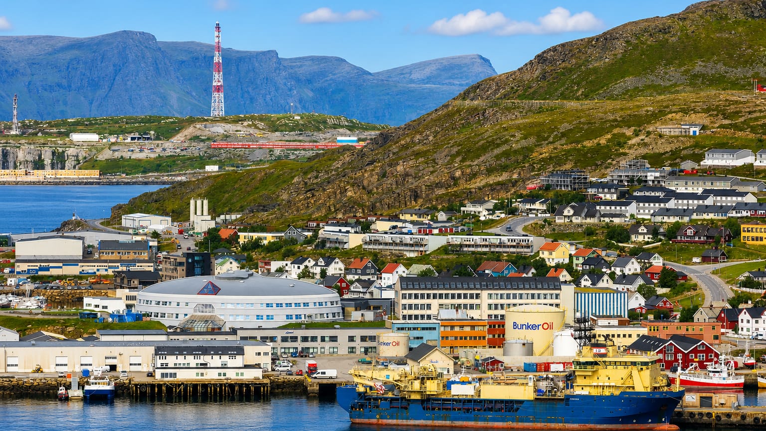 Waterfront town of Hammerfest, Norway, below barren mountains with harbour vessels and a radio mast