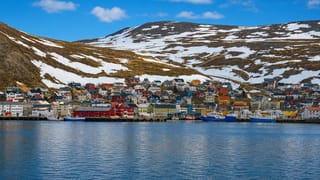 Honningsvag's colorful harbor houses and fishing boats below a snow-patched Arctic hill in Finnmark, Norway