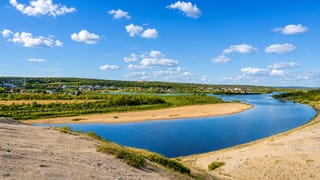 Broad sandy river bend below the tundra plateau with the settlement of Kautokeino, Norway beyond.
