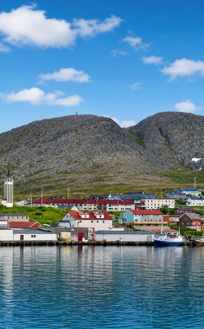 Colourful houses and fishing boats of Mehamn, Norway, along the harbour below bare Arctic mountains