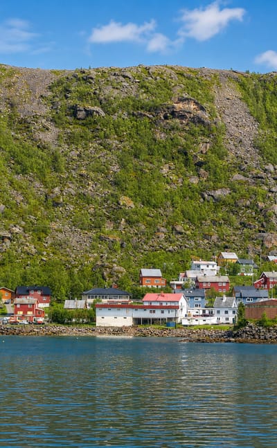 Øksfjord, Norway, its waterfront houses clustered beneath a steep green mountain along the fjord.