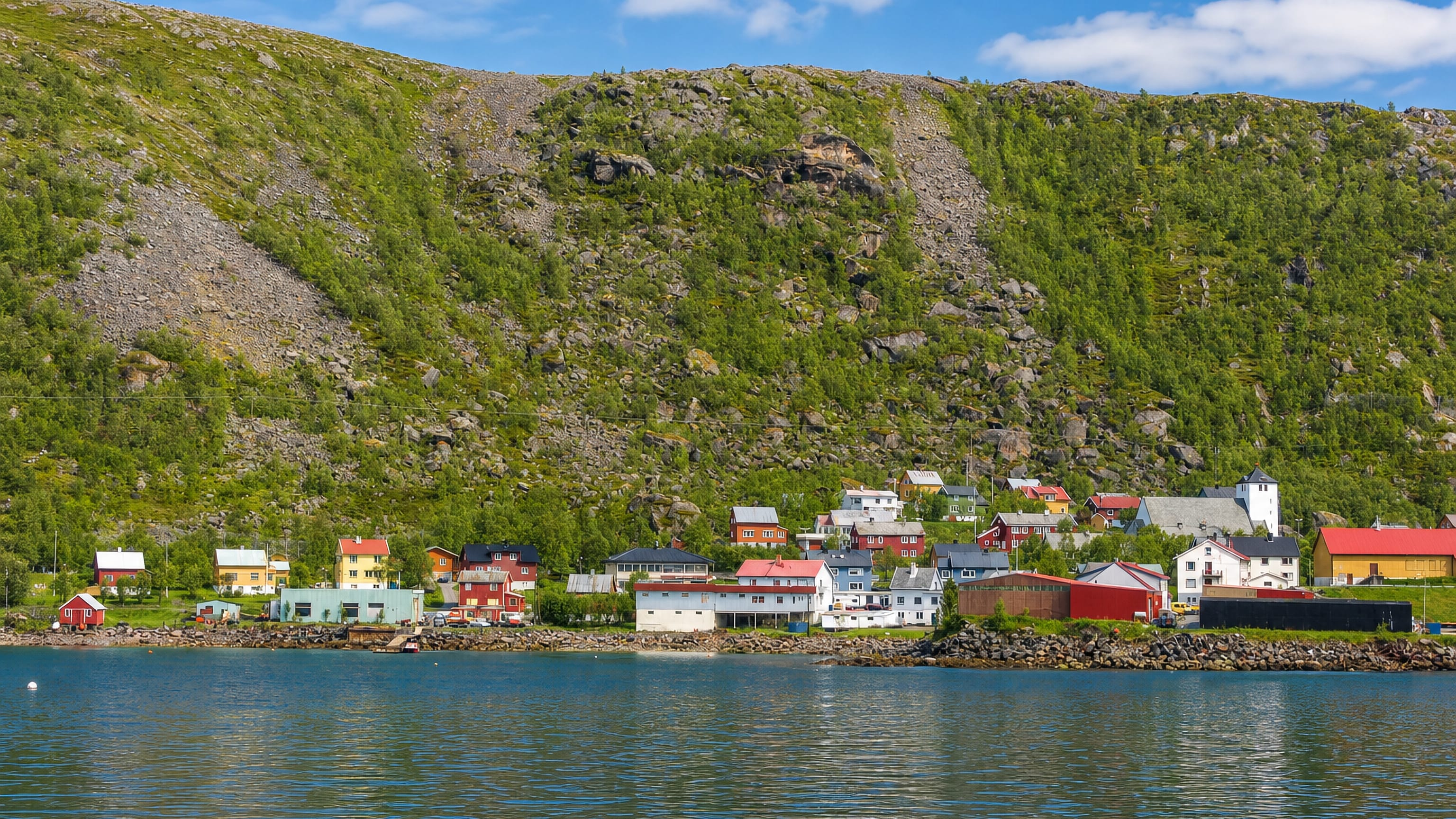 Øksfjord, Norway, its waterfront houses clustered beneath a steep green mountain along the fjord.