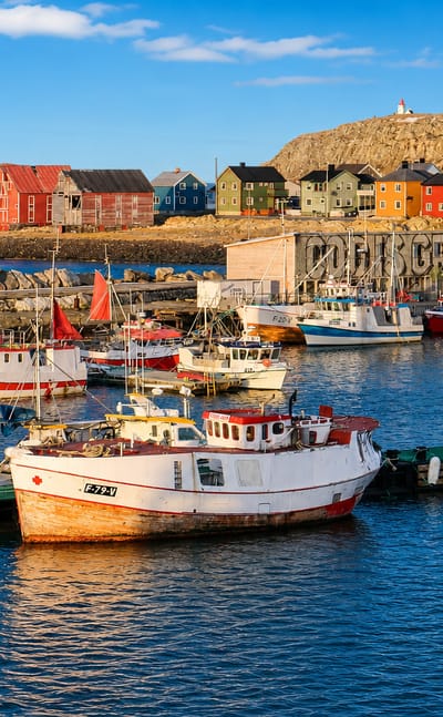 Colourful fishing boats and painted harbour houses below the lighthouse hill at Vardo, Norway.