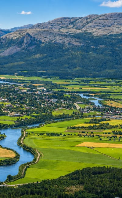 Aerial view of Alvdal, Norway, with the Glomma river winding through green farmland below forested mountains