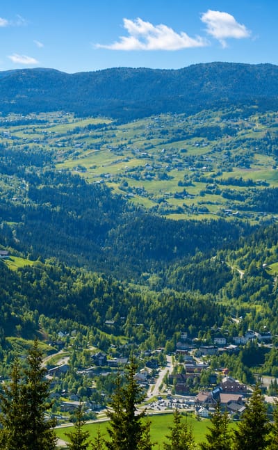 Bagn village nestled on the floor of a green, forested Valdres valley ringed by wooded hills under a blue summer sky.