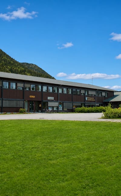 Brown-timber municipal building at Bergset with a lawn, statue and forested mountain rising behind