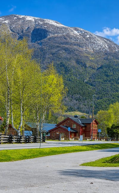 Traditional red timber cabins and birch trees below a snow-capped mountain in Bismo, Norway.