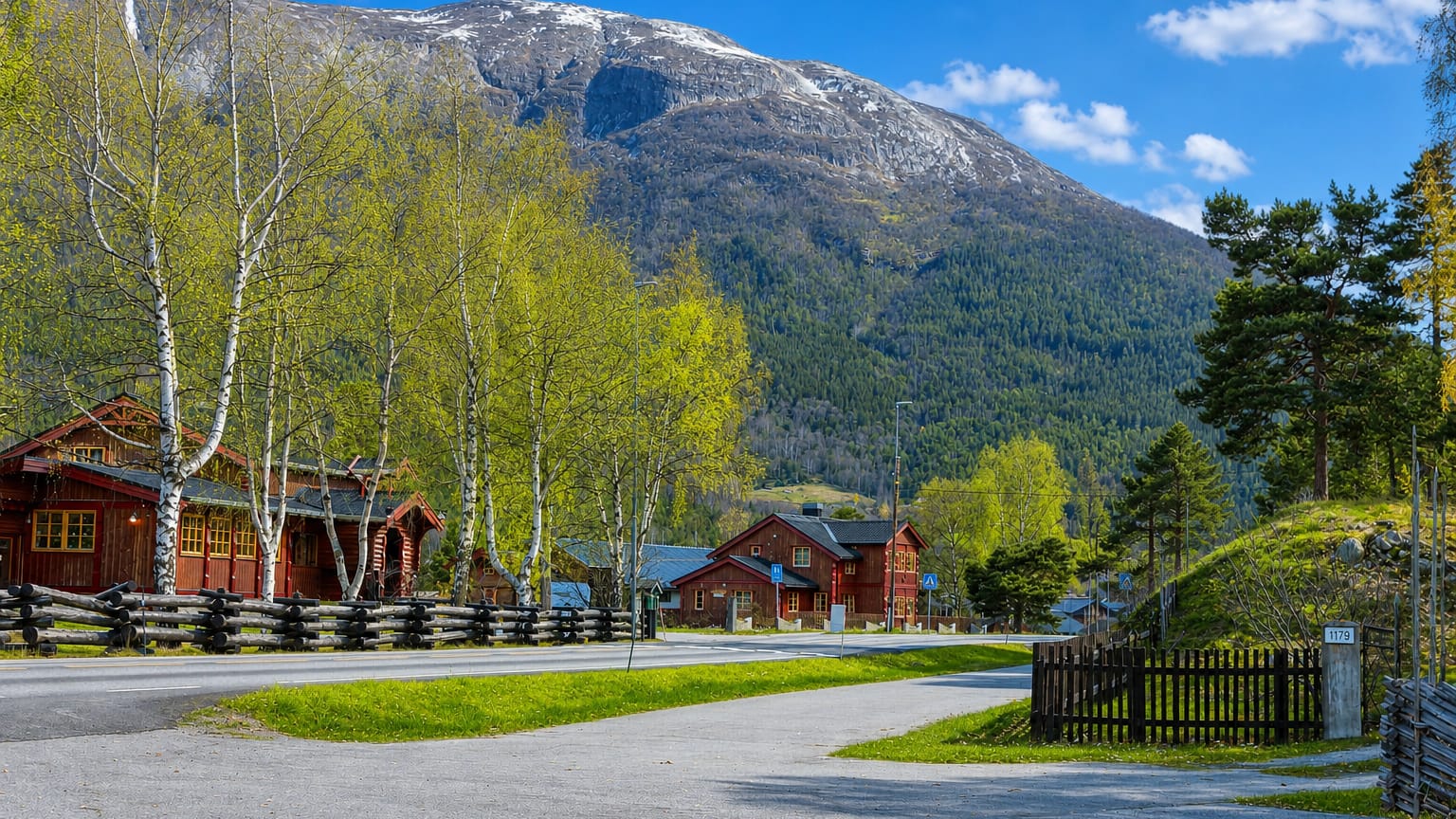 Traditional red timber cabins and birch trees below a snow-capped mountain in Bismo, Norway.