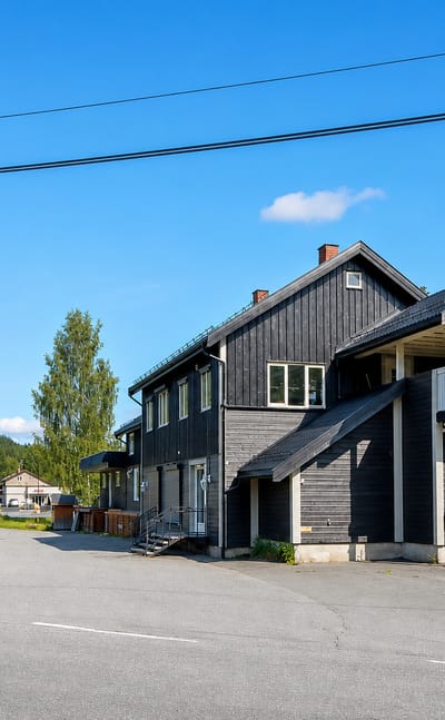 A dark timber building and quiet street in the village of Bruflat, Innlandet, Norway, under clear skies.