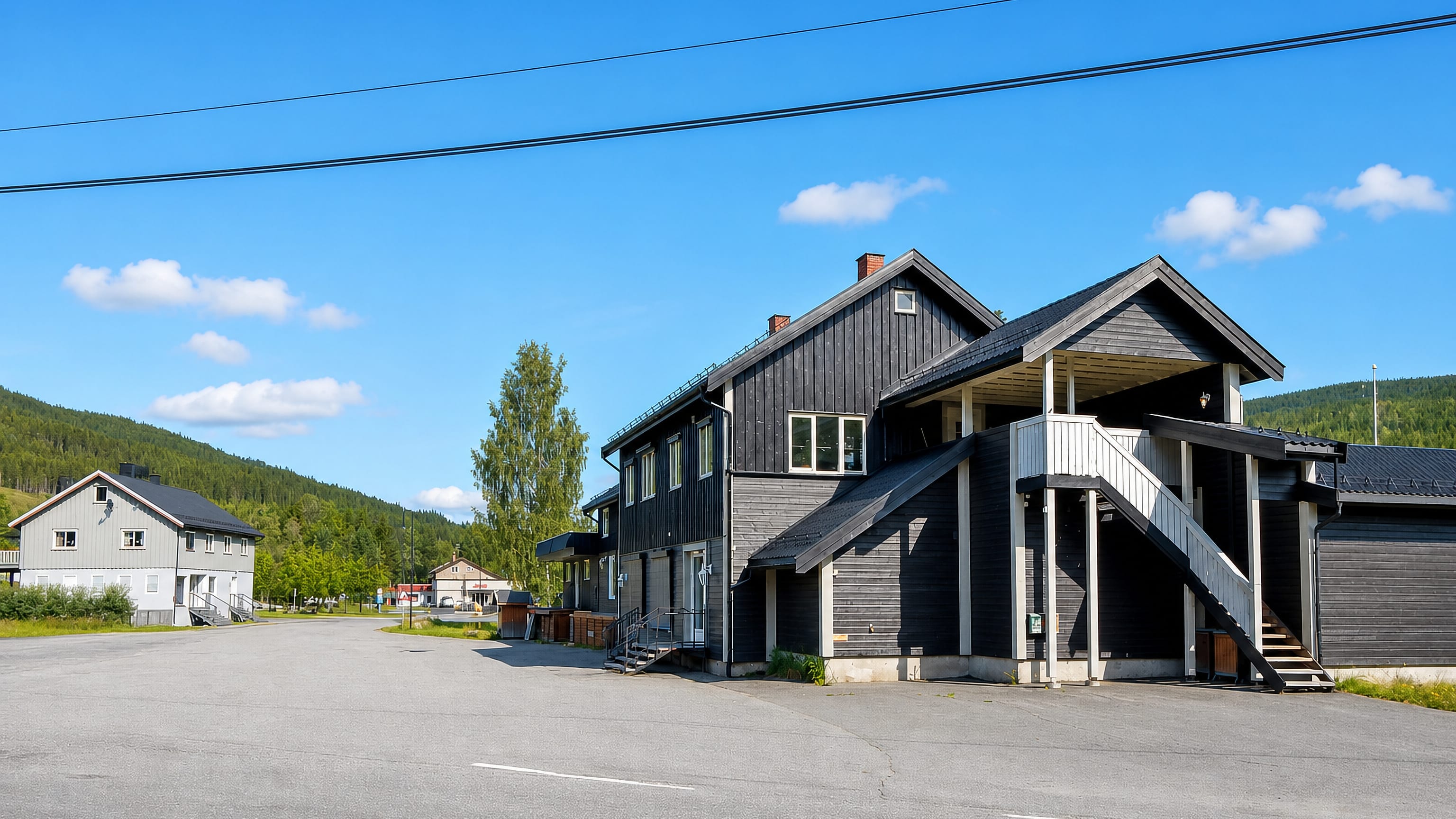 A dark timber building and quiet street in the village of Bruflat, Innlandet, Norway, under clear skies.