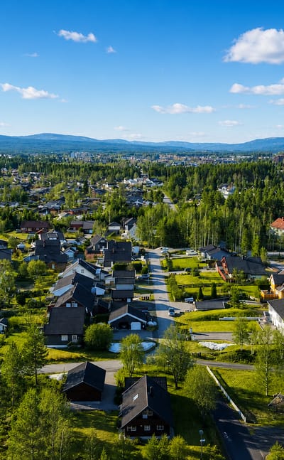 Aerial view of residential Elverum, Norway, spread among forest and distant blue hills under a clear sky