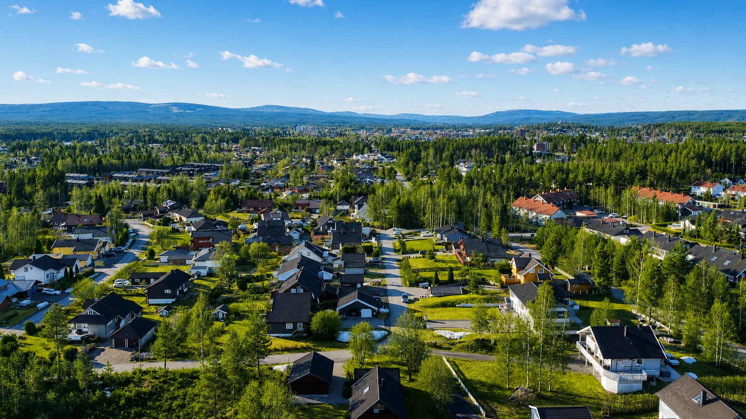 Aerial view of residential Elverum, Norway, spread among forest and distant blue hills under a clear sky