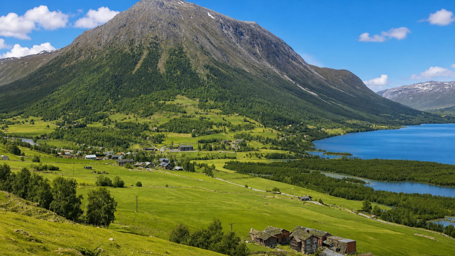 Green mountain valley at Fossbergom, Norway, with scattered farms and turf-roofed buildings beside a lake below a steep peak.