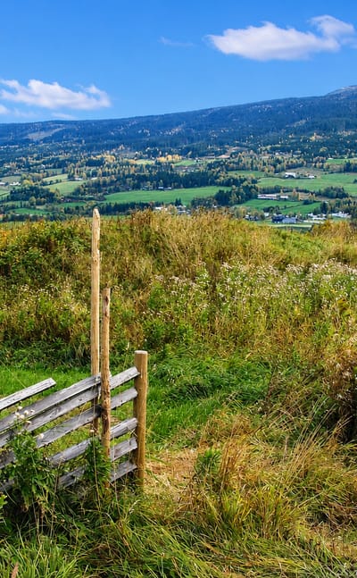 View over Hundorp's Gudbrandsdalen valley with farmland, a river and forested hills, framed by a traditional wooden rail fence