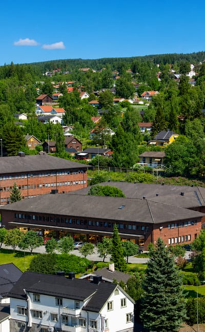 Aerial view of brick civic buildings and houses among green forest in Jaren, Innlandet, Norway