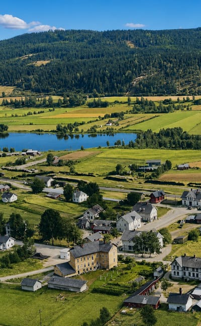 Aerial view over Kirkenær, Norway, scattered houses among green farmland with a small lake and forested hills