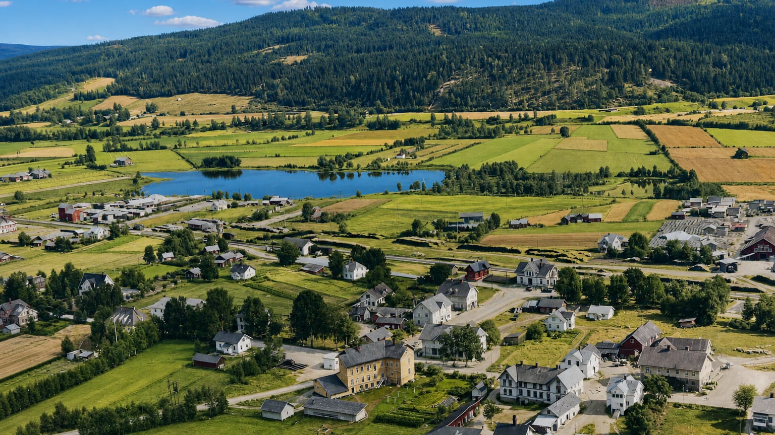 Aerial view over Kirkenær, Norway, scattered houses among green farmland with a small lake and forested hills