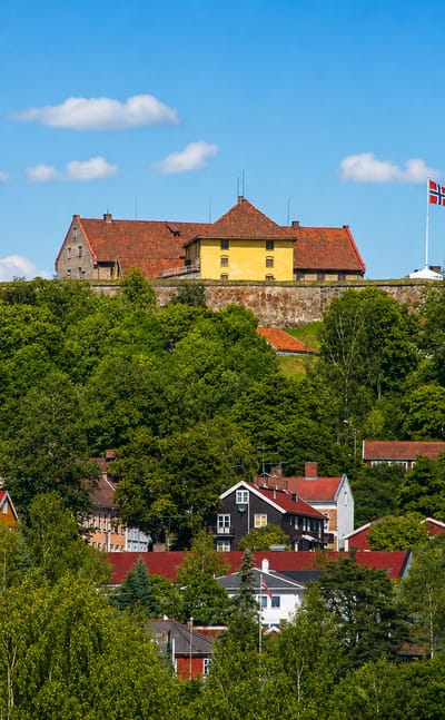 Kongsvinger Fortress flying the Norwegian flag on a wooded hill above the colorful wooden houses of Kongsvinger, Norway