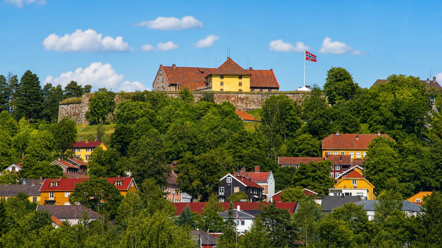 Kongsvinger Fortress flying the Norwegian flag on a wooded hill above the colorful wooden houses of Kongsvinger, Norway
