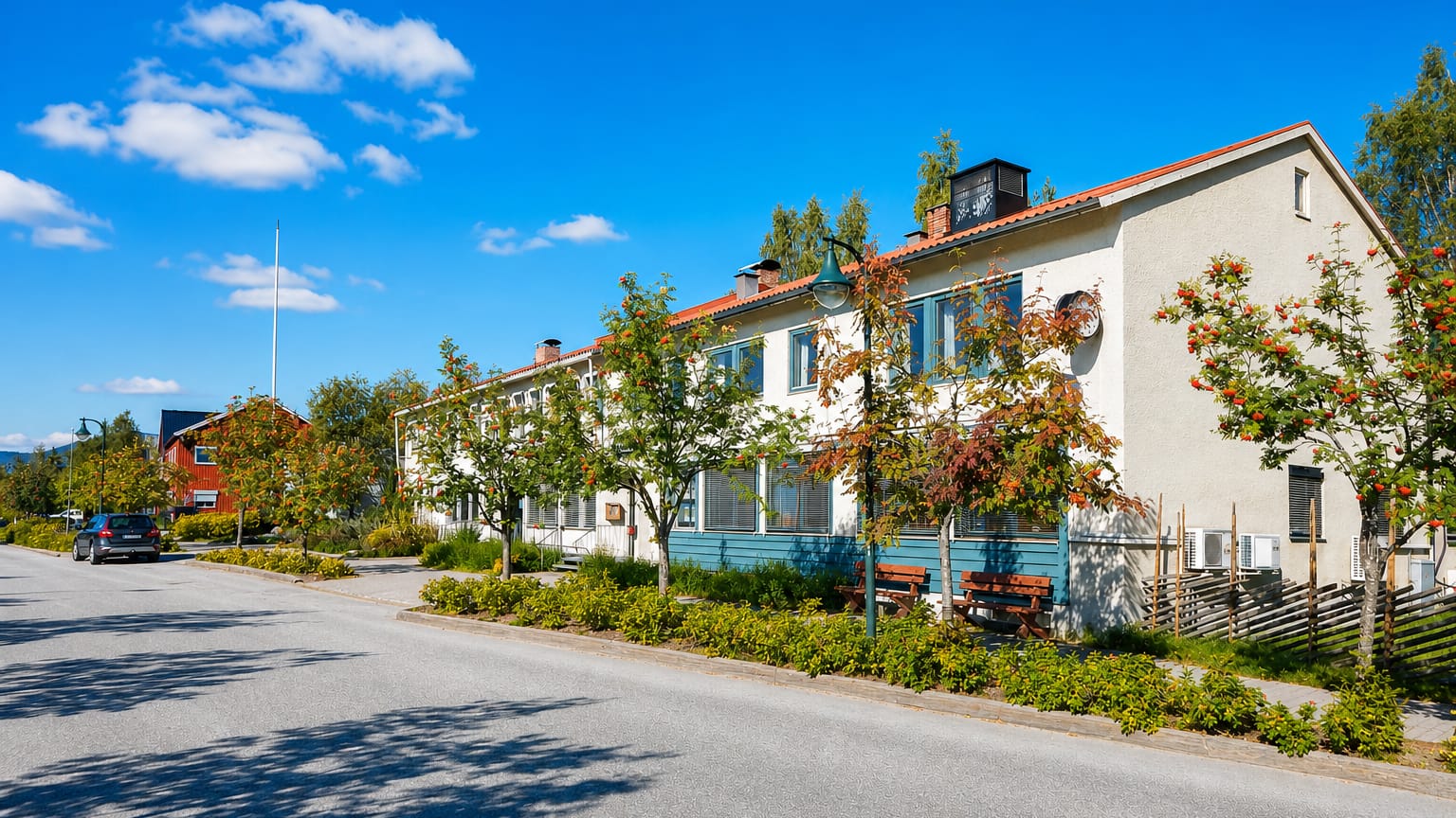Quiet street with a long timber building and berry-laden rowan trees in Koppang, Norway