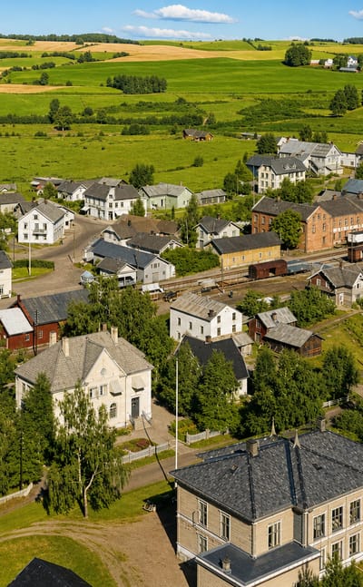 Aerial view of Løten village in Innlandet, Norway, with white and red wooden houses, a railway line and green farmland.