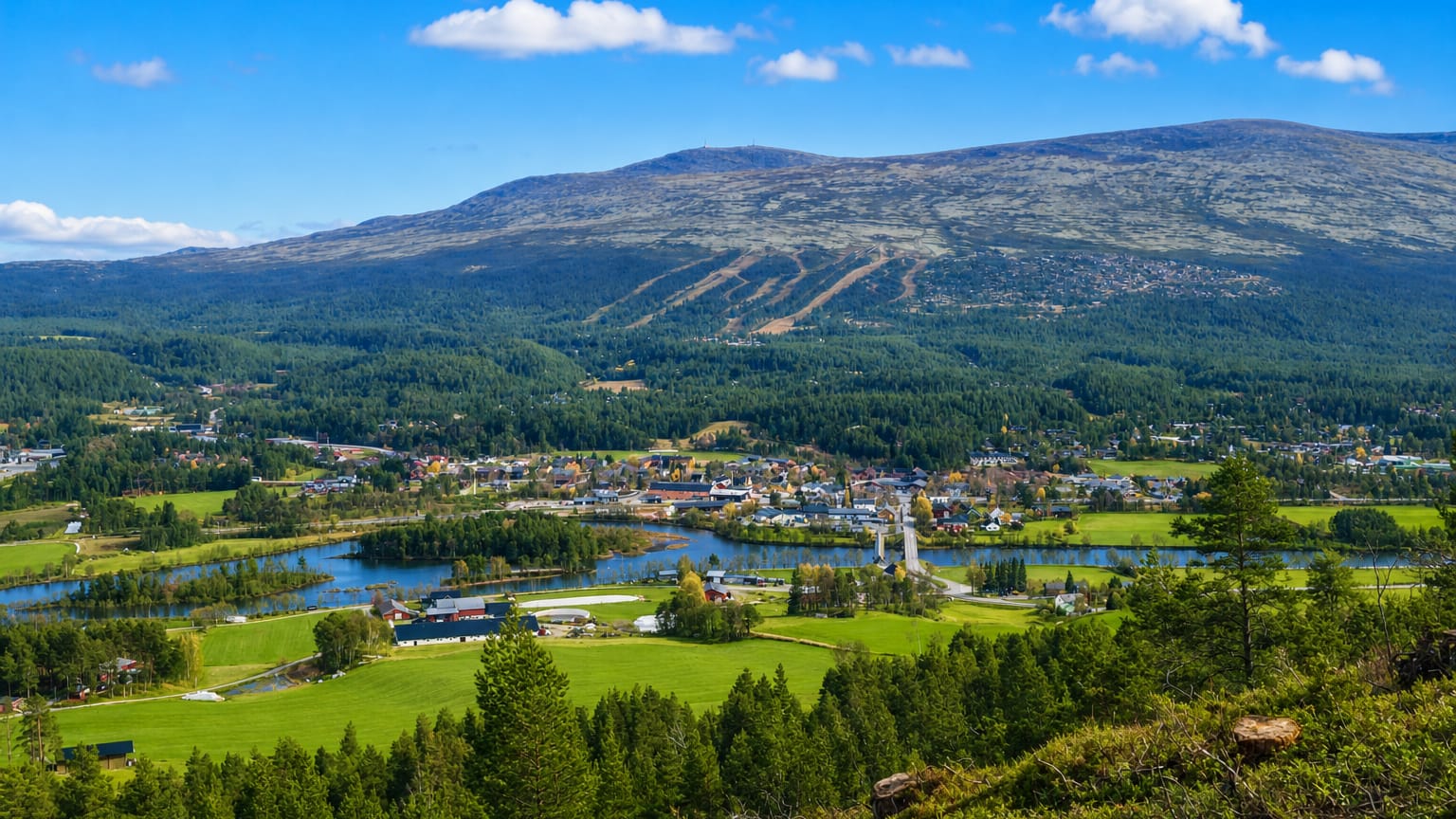 Valley view of Os, Norway, with a village by a lake, green fields and a ski-marked mountain behind