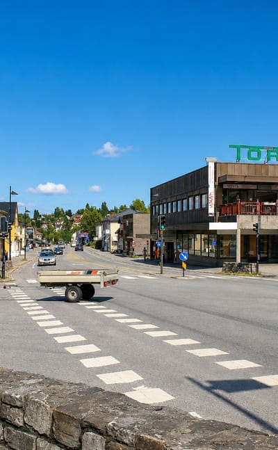 Street junction in Raufoss with a modern shopping building marked Torvet, a parked car and crosswalk.