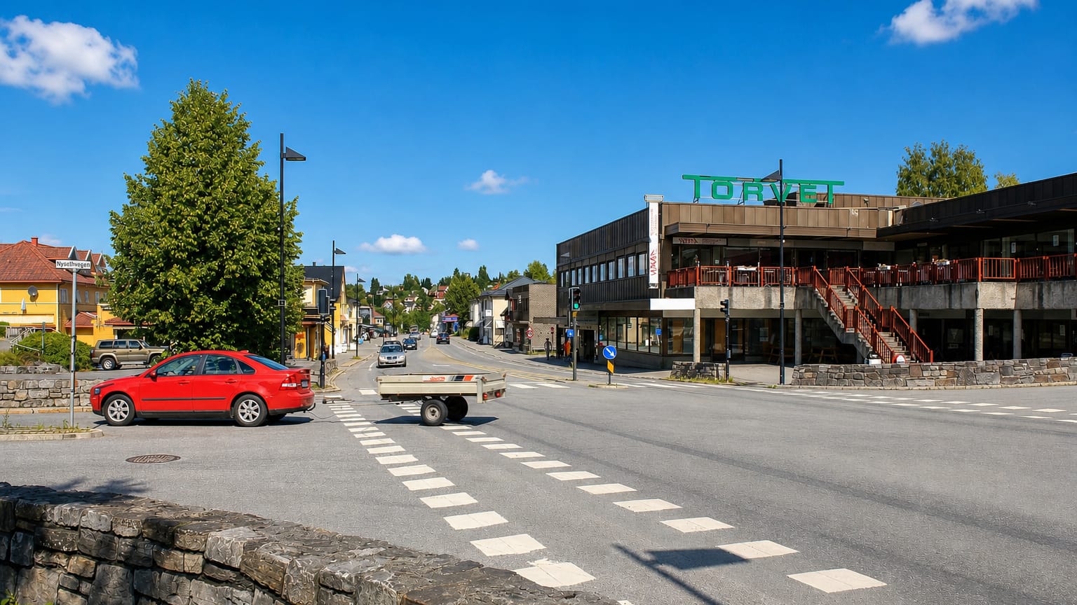 Street junction in Raufoss with a modern shopping building marked Torvet, a parked car and crosswalk.