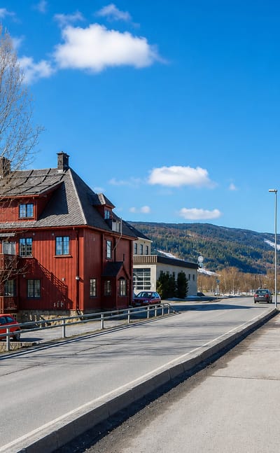 Red wooden building along the main street of Segalstad bru with a road sign and wooded hills behind