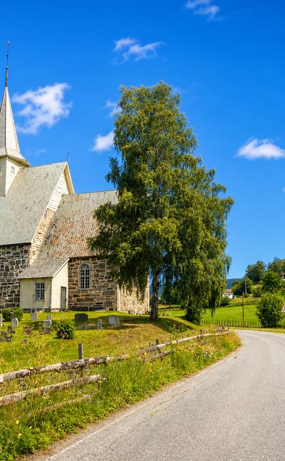 Medieval stone church and churchyard at Slidre beside a country lane amid green fields and birch trees
