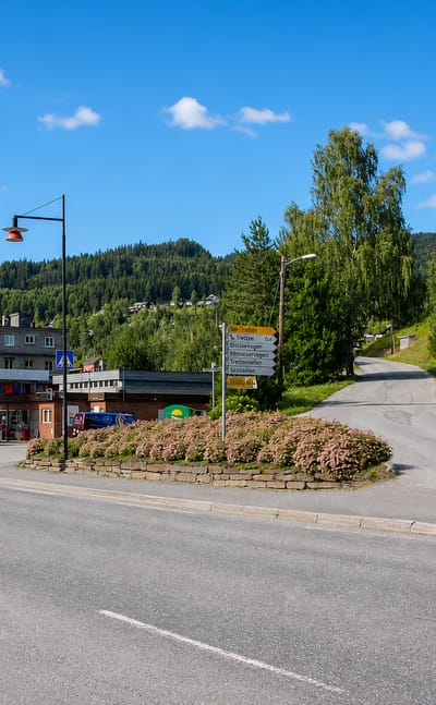 Tretten, Norway, a village road junction with signposts and shops below forested Gudbrandsdalen hills.
