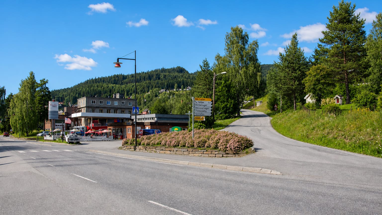 Tretten, Norway, a village road junction with signposts and shops below forested Gudbrandsdalen hills.